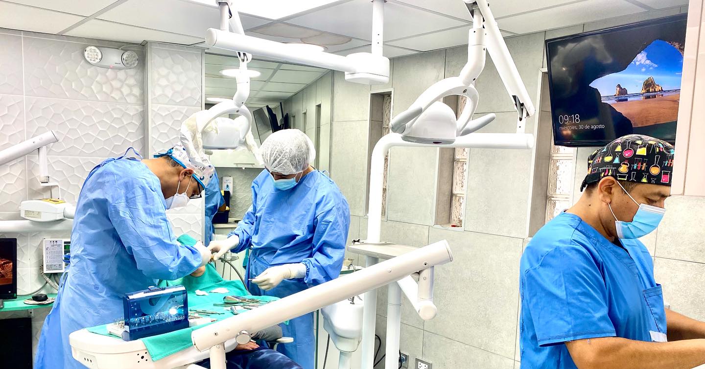 Tres odontólogos con mascarilla y uniforme quirúrgico atienden a un paciente en un consultorio de la clínica