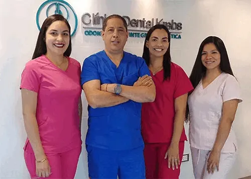 El equipo de Clínica Dental Krebs: un odontólogo con uniforme azul y tres odontólogas frente al logo de la clínica