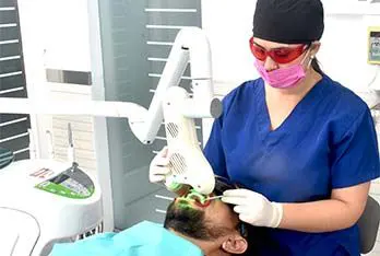 Odontóloga con gafas de protección aplicando blanqueamiento láser a un paciente