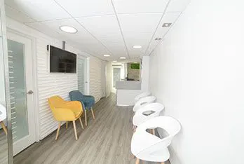 Sala de espera con sillas blancas, amarilla y azul y un televisor